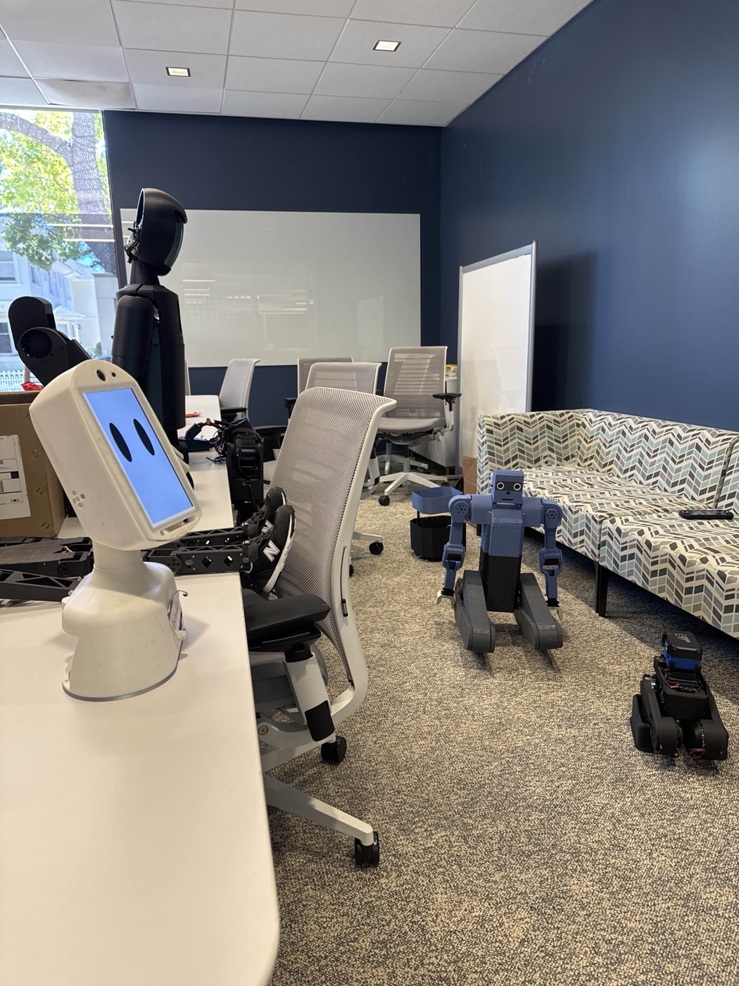 Home-built robots lined up — humanoid, telepresence bot, and a blue quadruped